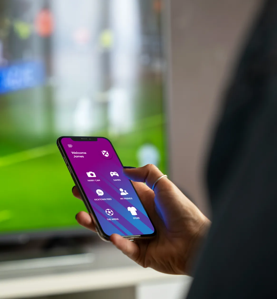 Person holding a phone showing the KickTown app home screen, with the football arena visible behind them